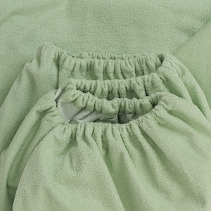 May include: A close-up of a light green fitted sheet with elastic edging. The sheet is made of a soft, textured fabric.