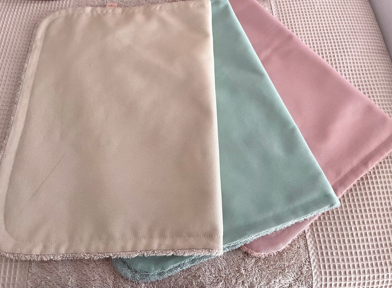 K&ouml;nnte beinhalten: Drei Stoffquadrate mit Fransen. Die Quadrate sind beige, hellgr&uuml;n und hellrosa.