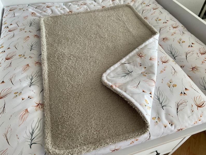 K&ouml;nnte beinhalten: Ein beiger Wickelauflagenbezug mit wei&szlig;em Blumenmuster. Der Bezug ist aus weichem, saugf&auml;higem Material gefertigt und sch&uuml;tzt Ihre Wickelauflage perfekt vor Versch&uuml;ttungen und Flecken.