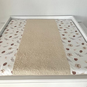 May include: A white changing pad cover with a beige, fluffy, textured center and two side panels with a white background and a brown floral pattern.