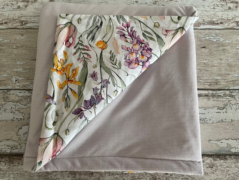 May include: A gray and white floral patterned blanket with a soft, textured surface. The blanket is folded in half, revealing the floral pattern.