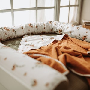 May include: A white and orange baby nest with a rainbow pattern and a brown blanket inside.