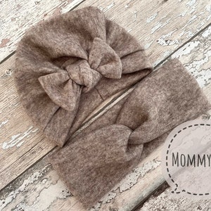 May include: A brown knitted headband with a large bow. The headband is on a wooden surface. The text "Mommy & Me" is visible in the image.