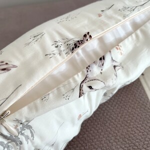 May include: A white pillowcase with a nature-themed print featuring birds and botanical elements in shades of gray, brown, and pink. The pillowcase has a zipper closure and is made of a soft, light-colored fabric.