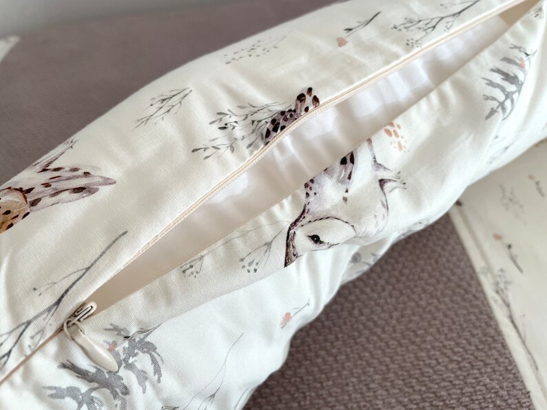May include: A white pillowcase with a nature-themed print featuring birds and botanical elements in shades of gray, brown, and pink. The pillowcase has a zipper closure and is made of a soft, light-colored fabric.
