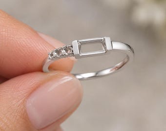 以下が含まれることがあります： バゲットカットの石を留めるための長方形の台座が中央にあり、片側に3つの小さな円形の爪が並んだシルバーカラーのリング。磨き上げられた金属製のバンドが、洗練された滑らかな外観を演出しています。
