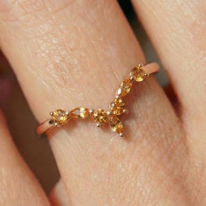 Può includere: Un anello a forma di V in oro rosa, caratterizzato da una serie di cinque piccole pietre preziose di citrino giallo dorato sfaccettate, disposte con un motivo a taglio marquise e rotondo lungo la curva superiore della fascia.
