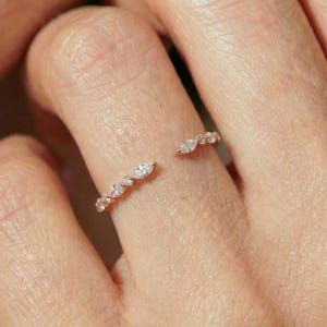 May include: A delicate open ring with a gold band, adorned with a series of small, sparkling diamonds. The ring features a unique design with a gap, showcasing the diamonds' brilliance. The ring is a piece of jewelry.