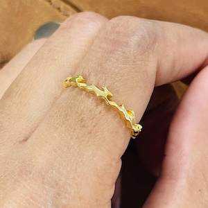 Puede incluir: Un anillo de color dorado con un diseño único, orgánico y texturizado. El anillo está hecho de una banda delgada de metal que está formada en una serie de curvas irregulares y fluidas.