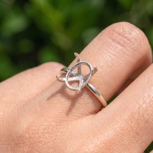 Könnte beinhalten: Eine silberfarbene Ringfassung mit einer leeren, ovalen Korbhalterung und vier Krappen, die für die Aufnahme eines Edelsteins ausgelegt ist. Die Metallschiene ist glatt und poliert und zeigt eine einfache Struktur für eine individuelle Fassung.