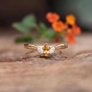 Peut inclure: Une bague en or avec une citrine jaune centrale taille marquise, entourée de deux petites pierres blanches transparentes taille marquise de chaque côté. L'anneau présente un design incurvé en forme de V maintenant les pierres.