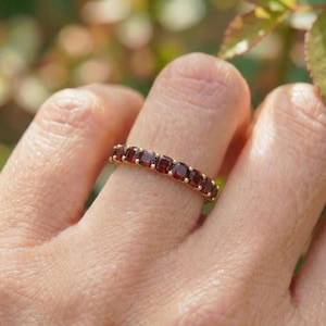 Op de afbeelding: Een gouden ring met een rij vierkant geslepen, dieprode edelstenen. De ring is gezet in een geelgouden band, wat een klassiek en elegant ontwerp creëert. De edelstenen zijn gelijkmatig verdeeld.