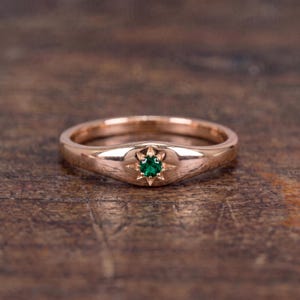 Könnte beinhalten: Ein Ring aus Roségold mit einem runden, grünen Edelstein, der in eine sternförmige Gravur eingefasst ist. Die Ringschiene ist glatt und poliert, wobei das Sternmotiv mittig auf der Vorderseite des Rings platziert ist und den Kontrast betont.