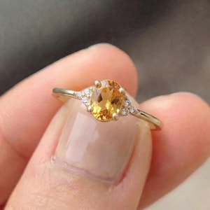 Könnte beinhalten: Ein Goldring mit einem zentralen, oval geschliffenen gelben Citrin-Edelstein. Die Fassung enthält drei kleine, klare, rund geschliffene Akzentsteine auf jeder Seite des Mittelsteins, montiert auf einer dünnen, polierten Goldschiene mit vier Krappen.