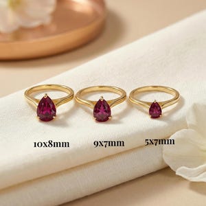May include: Three gold rings, each featuring a single pear-cut deep red gemstone. The rings are labelled with sizes 10x8mm, 9x7mm, and 5x7mm, indicating the dimensions of the teardrop-shaped stones set in polished yellow gold bands.