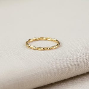 May include: A thin, circular ring crafted from polished yellow gold, featuring a continuous twisted rope texture that wraps around the entire circumference of the band, creating a uniform and repeating spiral pattern throughout the metal surface.