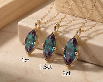 Op de afbeelding: Drie gouden kettingen met van kleur veranderende edelstenen in marquise-slijpvorm in klauwzettingen. De hangers zijn gelabeld met 1ct, 1.5ct en 2ct, wat hun respectievelijke grootte aangeeft. De stenen vertonen een verloop van blauwgroene, groene en paarse tinten.