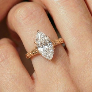 May include: A gold engagement ring with a large, marquise-cut diamond. The ring has an intricate, engraved design on the band. The diamond is set with prongs and sparkles brightly.