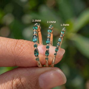 Op de afbeelding: Drie gouden ringen met afwisselend marquise- en rondgeslepen groene edelstenen. De ringen zijn gelabeld met de maten 2,5 mm, 2,0 mm en 1,5 mm, wat de breedte van de banden aangeeft. Elke ring toont een verfijnde, symmetrische opstelling van stenen.