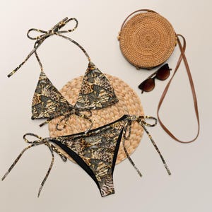 May include: A brown and black animal print bikini with a triangle top and a high-cut bottom. The bikini is on a woven straw mat with a round straw bag and sunglasses.
