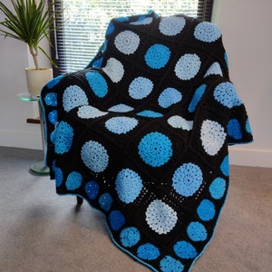 May include: A crocheted throw blanket with a black background and blue and white circles. The blanket is draped over a chair.