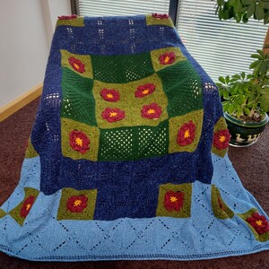 May include: A blue, green, and red crocheted throw blanket with a floral pattern. The blanket is made of soft yarn and has a fringed edge.