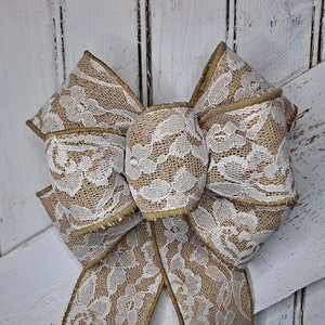 May include: A large, brown burlap bow with white lace overlay. The bow is tied with a long tail and is perfect for decorating a door or wreath.