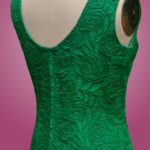 Puede incluir: Un vestido verde esmeralda sin mangas con un estampado de rosas. El vestido tiene un escote redondo y una silueta ajustada.