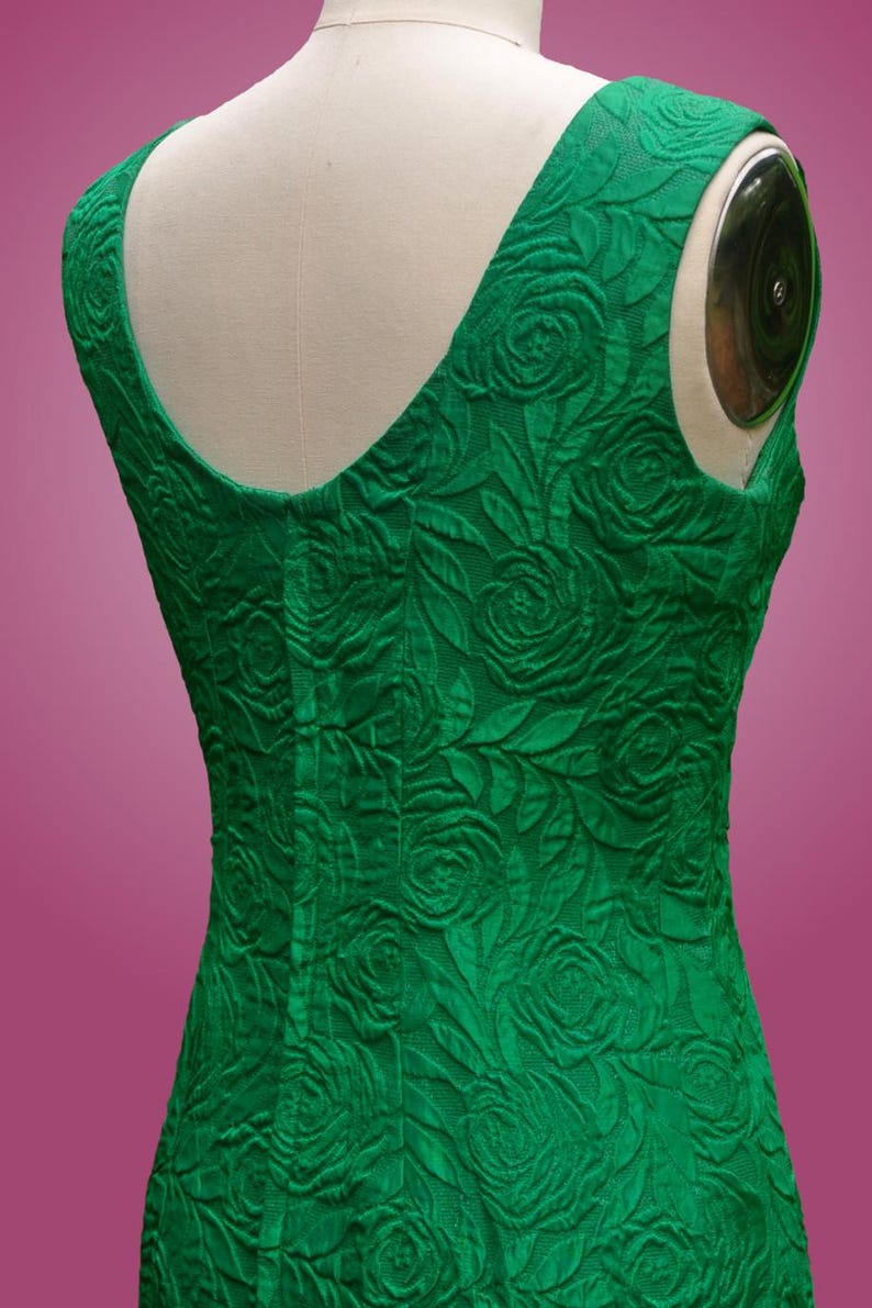 Puede incluir: Un vestido verde esmeralda sin mangas con un estampado de rosas. El vestido tiene un escote redondo y una silueta ajustada.