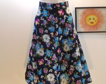 May include: A black midi skirt with a floral print featuring blue, white, and pink flowers. The skirt has a flared silhouette and a high waist.