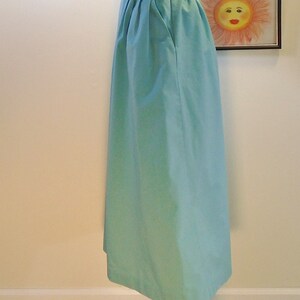 May include: A light blue midi skirt with a single button closure at the waist. The skirt has pleats at the front and a single pocket on the right side.