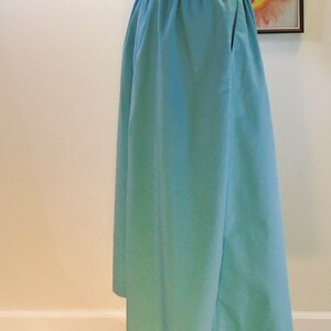 May include: A light blue, full-length skirt with a gathered waistband and a single pocket on the right side.