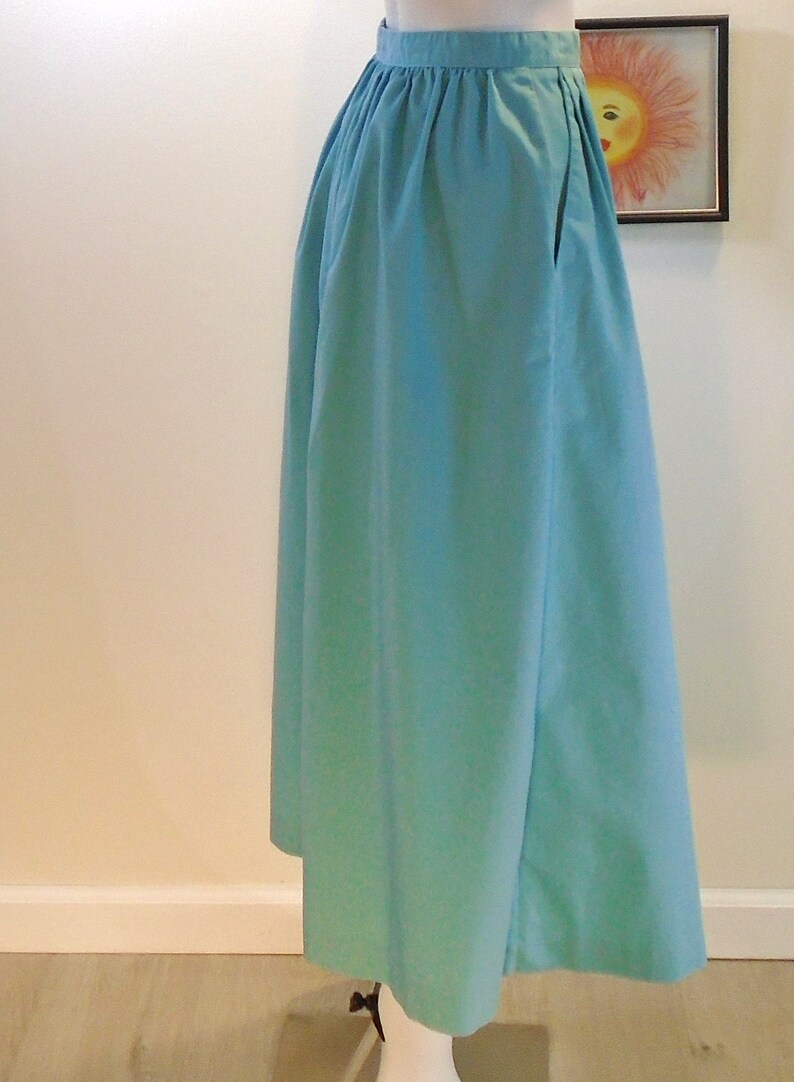 May include: A light blue, full-length skirt with a gathered waistband and a single pocket on the right side.