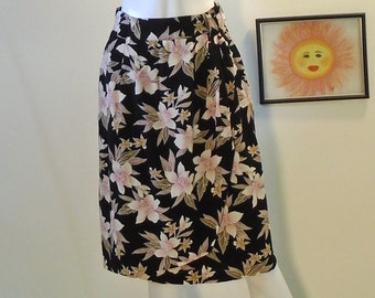 May include: A black wrap skirt with a floral print featuring pink and brown flowers. The skirt has a tie at the waist.