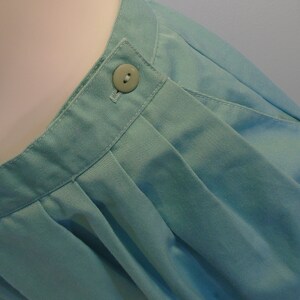 May include: A light blue skirt with a single button at the waist. The skirt is pleated and has a smooth, cotton-like texture.