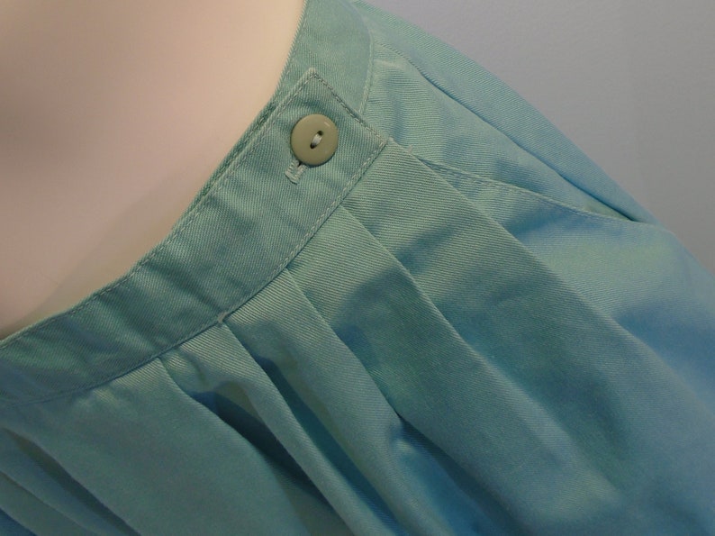 May include: A light blue skirt with a single button at the waist. The skirt is pleated and has a smooth, cotton-like texture.