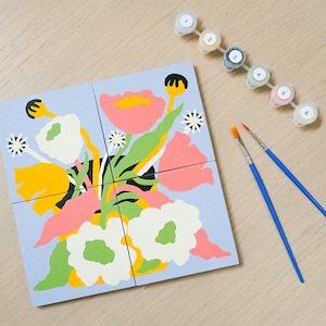 May include: A paint-by-numbers kit with a floral design. The artwork is split into four squares, with pink, yellow, white, and green flowers on a pale blue background. Includes paint pots and two paintbrushes.