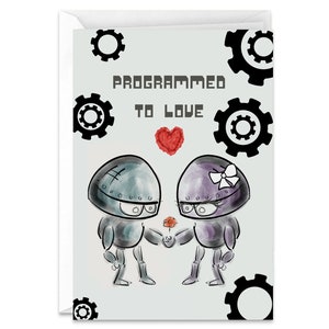 May include: A greeting card with a cartoon illustration of two robots holding a red flower. The text on the card reads "Programmed to Love" with a red heart.