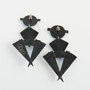 Może przedstawiać: Para czarnych geometrycznych kolczyk&oacute;w z srebrnym zapięciem. Kolczyki wykonane są z wielu warstw tr&oacute;jkąt&oacute;w i mają unikalny, nowoczesny design.