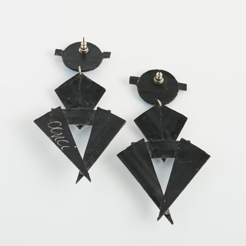 Może przedstawiać: Para czarnych geometrycznych kolczyk&oacute;w z srebrnym zapięciem. Kolczyki wykonane są z wielu warstw tr&oacute;jkąt&oacute;w i mają unikalny, nowoczesny design.