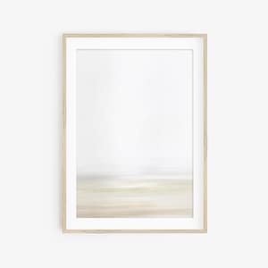 Puede incluir: Una pintura abstracta enmarcada con un marco de madera marrón claro. La pintura presenta un paisaje horizontal borroso con tonos de blanco, gris y beige.