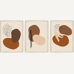 Puede incluir: Conjunto de tres impresiones de arte abstracto con formas marrones, naranjas y beige sobre un fondo crema. Las impresiones est&aacute;n enmarcadas en un marco de madera claro.