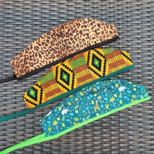 May include: Three surgical caps with different patterns. The top cap is brown with a leopard print. The middle cap is orange, green, and yellow with a geometric pattern. The bottom cap is teal with a green border and a pattern of palm trees, elephants, and giraffes.