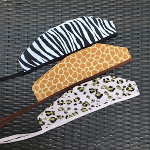 May include: Three fabric headbands with different animal print patterns. The headband on top has a black and white zebra print. The middle headband has a brown and orange giraffe print. The bottom headband has a pink and brown leopard print.