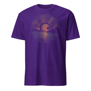 Man wearing a black t-shirt featuring a retro sunset illustration shaped like a vinyl record, showing palm trees, a glowing sun, and reflective ocean waves in warm orange and green tones.