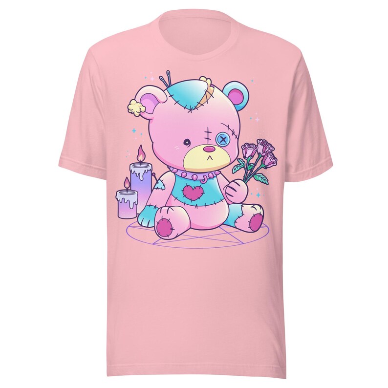 May include: A pink t-shirt with a cartoon image of a pink and blue stitched teddy bear holding a bouquet of pink roses. The bear is sitting on a pentagram with two purple candles.