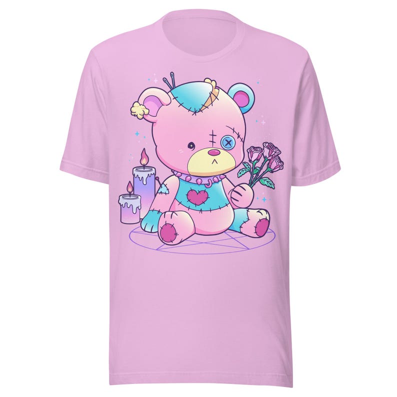 May include: A pink t-shirt with a cartoon image of a pink and blue stitched teddy bear holding a bouquet of pink roses. The bear is sitting on a pentagram with two candles behind it.