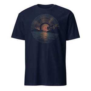 Man wearing a black t-shirt featuring a retro sunset illustration shaped like a vinyl record, showing palm trees, a glowing sun, and reflective ocean waves in warm orange and green tones.