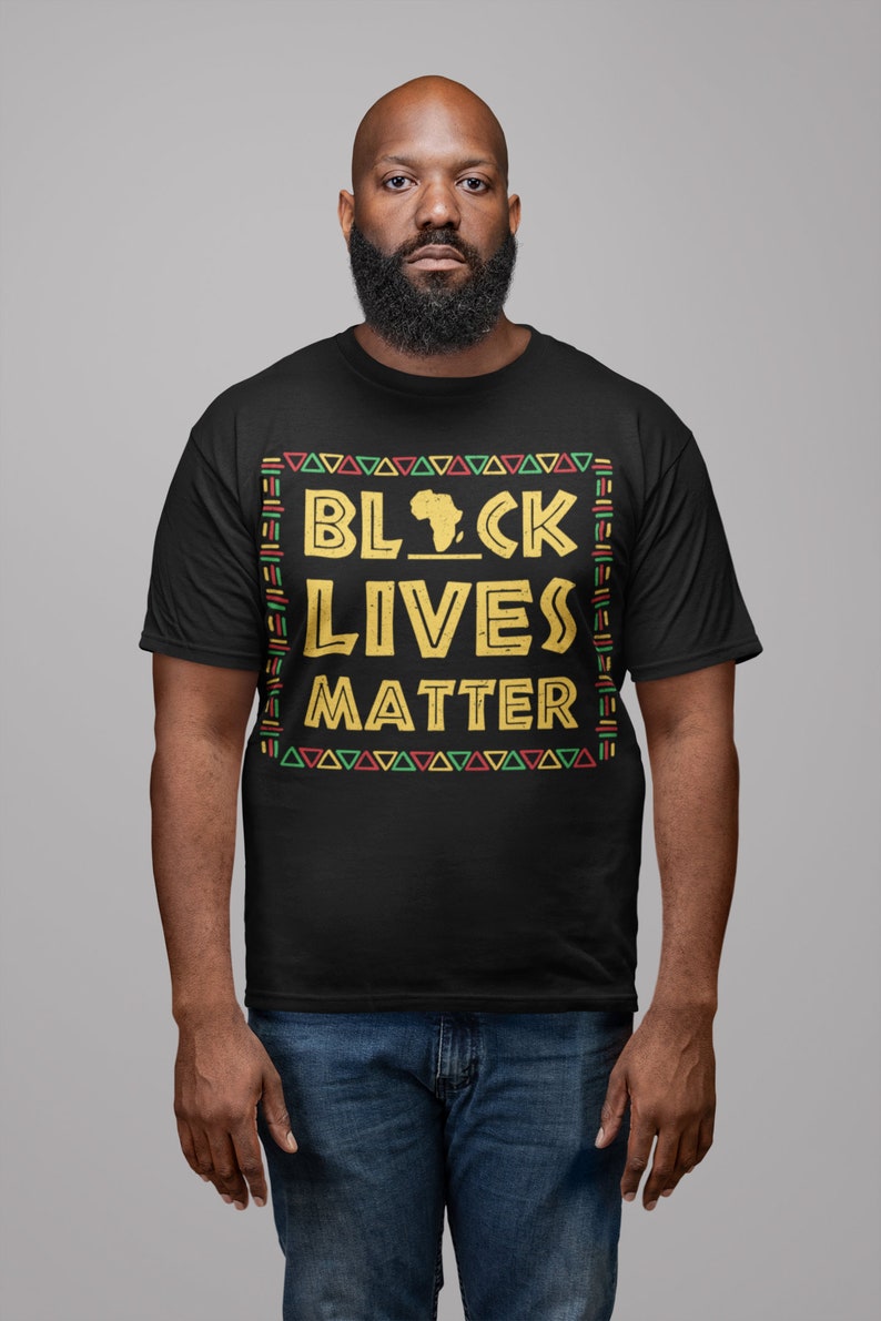 Peut inclure: Un t-shirt noir avec un motif dor&eacute; qui dit "Black Lives Matter" avec un contour du continent africain. Le motif est entour&eacute; d'un motif color&eacute; de triangles et de lignes.