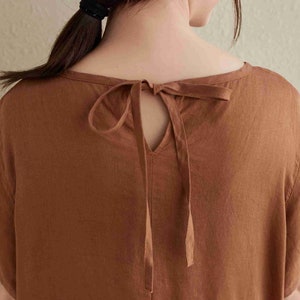 Puede incluir: Un vestido de lino marr&oacute;n con un escote de llave y un lazo en la espalda.